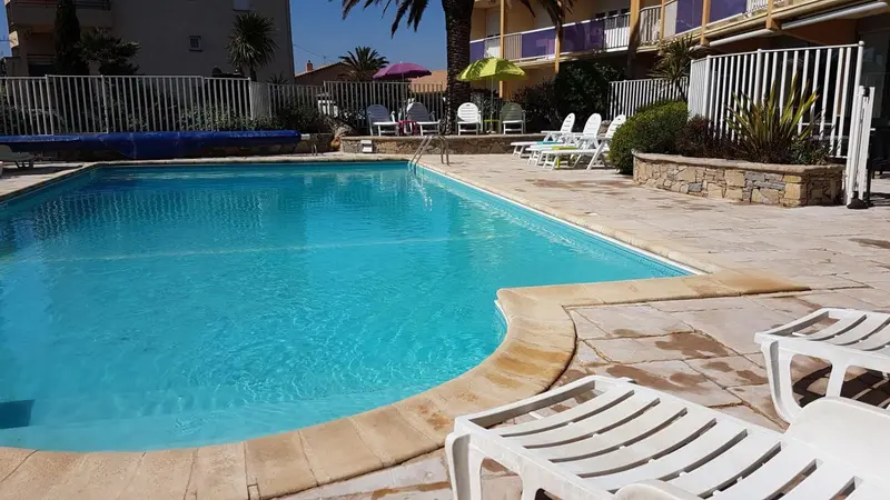 Une piscine rectangulaire bordée de transats blancs et de végétation.