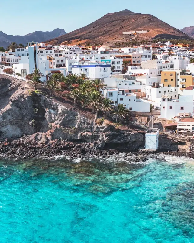 Vue d'un village blanc sur une colline surplombant la mer turquoise.