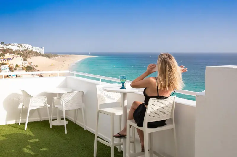 Une personne assise à une table sur une terrasse ensoleillée avec vue sur la mer.