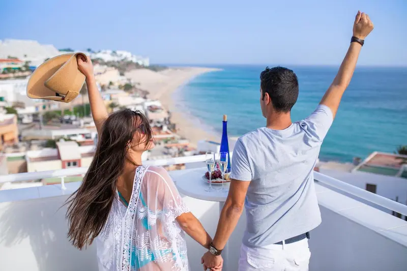 Un couple se tient la main sur une terrasse ensoleillée avec vue sur la mer.
