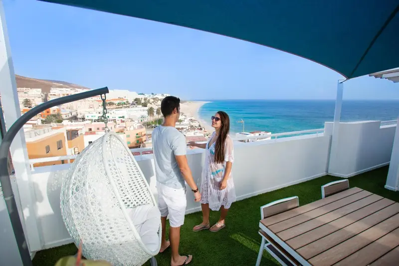 Un couple admire la vue depuis une terrasse ensoleillée.