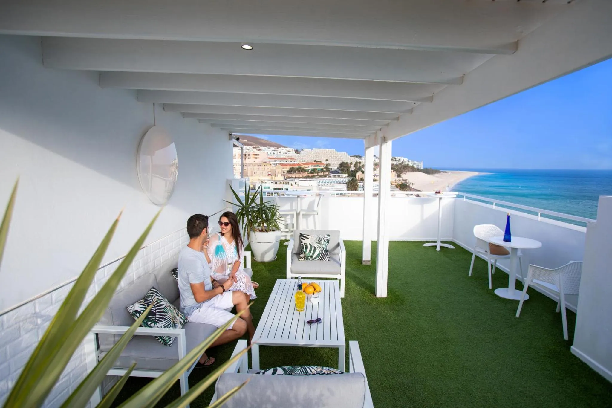 Un couple se détend sur une terrasse avec vue sur la mer et la ville.