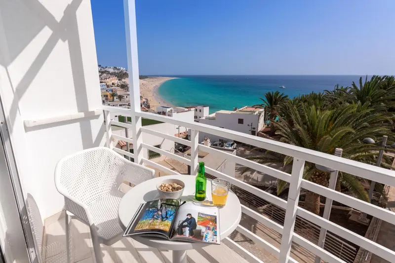 Une table et une chaise en plastique blanc sur un balcon avec vue sur la mer et la plage.