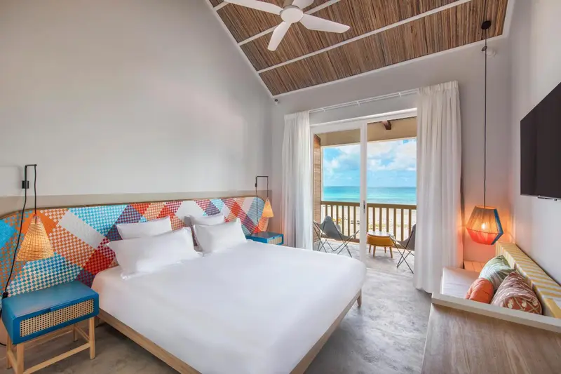 Chambre lumineuse avec un grand lit blanc donnant sur une terrasse et la mer.