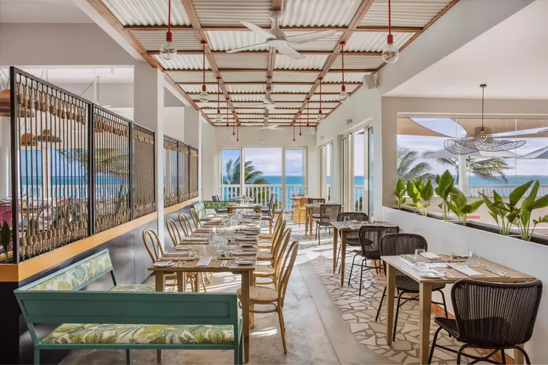 Une salle à manger lumineuse avec des tables dressées face à l'océan.