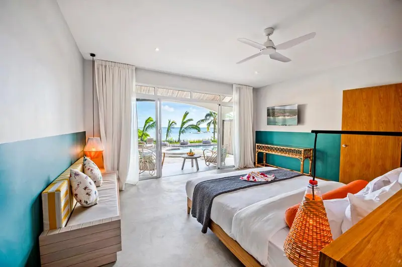Chambre lumineuse avec un lit double et vue sur la mer par de grandes baies vitrées.