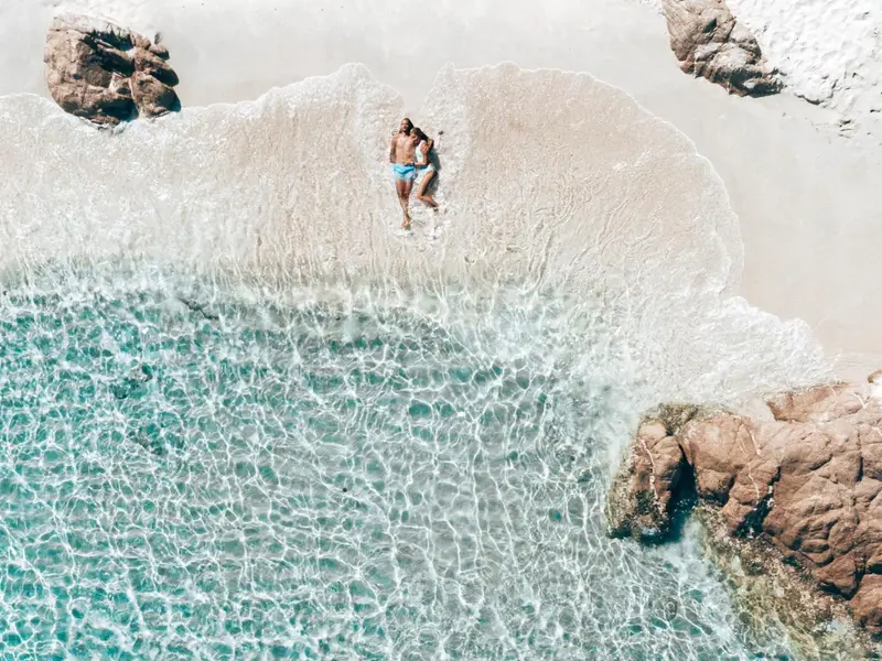 Vue aérienne d'un couple se relaxant dans les eaux turquoise d'une plage de sable blanc.