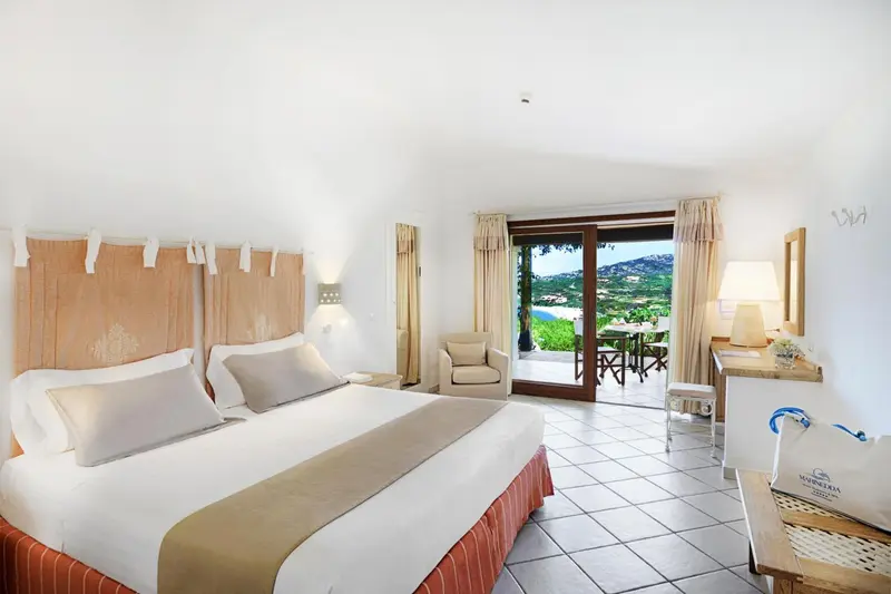 Chambre lumineuse avec un grand lit et une vue sur un paysage verdoyant.