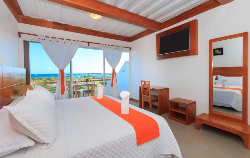 Chambre lumineuse avec lit fait et vue sur la mer par de grandes baies vitrées.