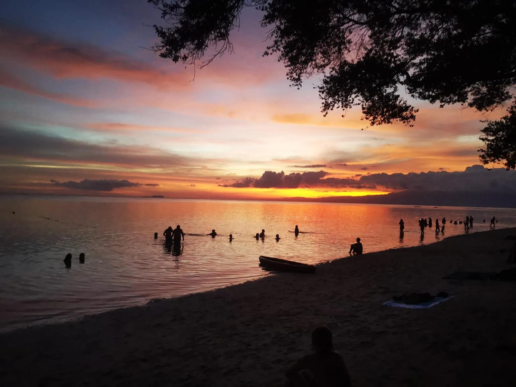 Coucher de soleil sur une plage avec des silhouettes de personnes dans l'eau.