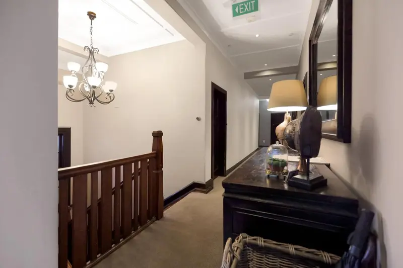 Un couloir d'hôtel clair avec un lustre et des lampes sur une console.