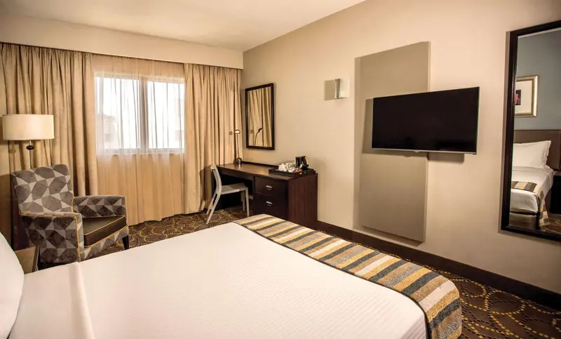 Une chambre d'hôtel lumineuse avec un lit, un bureau et un fauteuil.