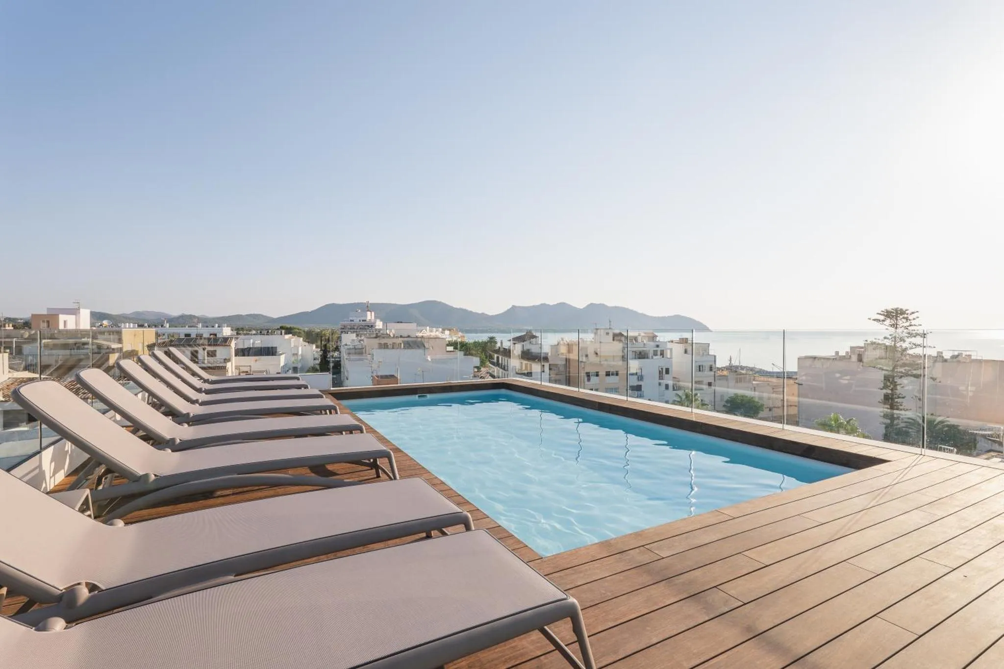 Transats alignés au bord d'une piscine sur une terrasse ensoleillée avec vue sur la mer et les montagnes.