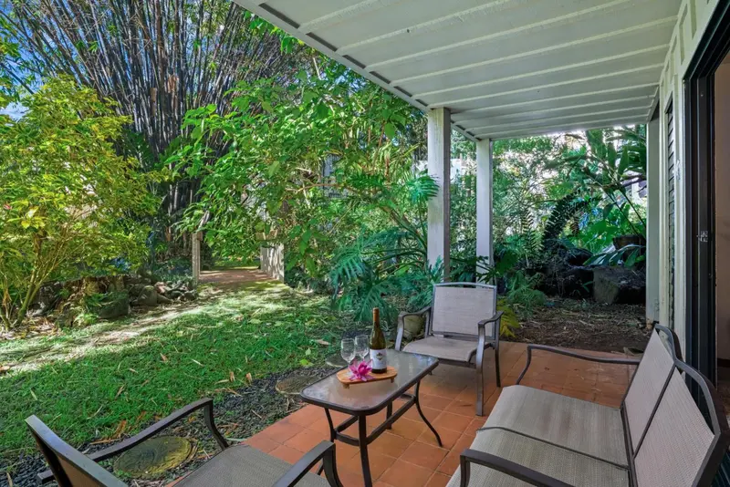 Une terrasse ombragée donne sur une végétation luxuriante et un jardin soigné.