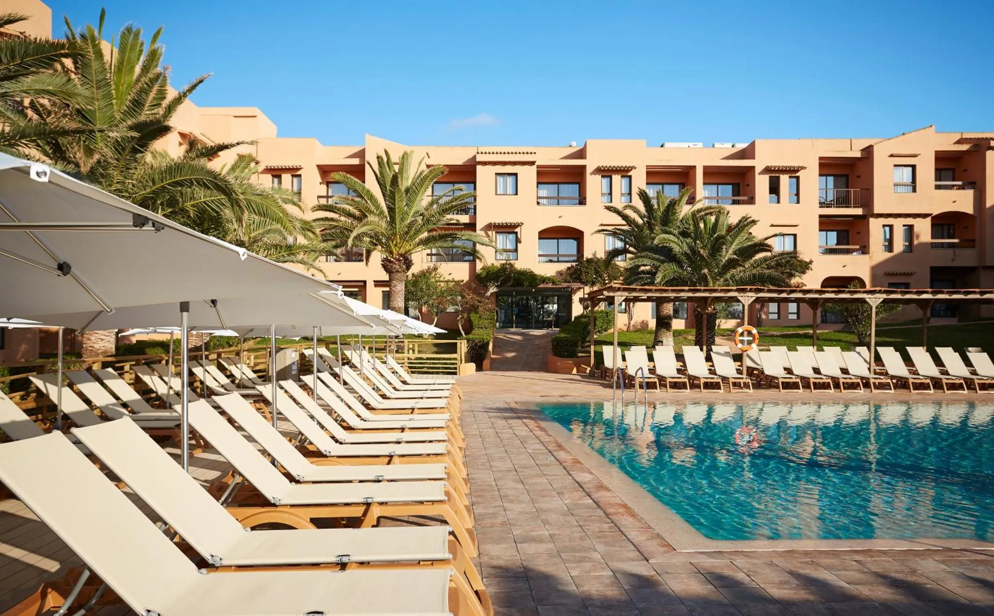Transats blancs alignés au bord d'une piscine turquoise dans un jardin tropical.