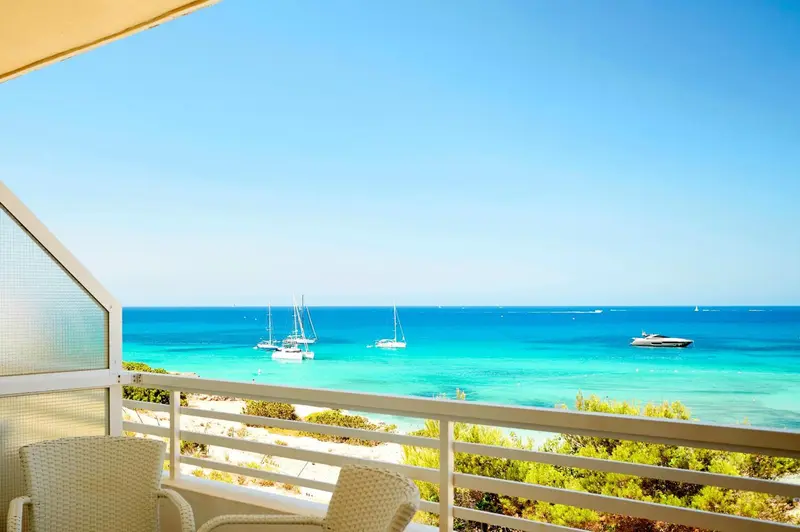 Vue sur la mer turquoise et les bateaux depuis une terrasse ensoleillée.