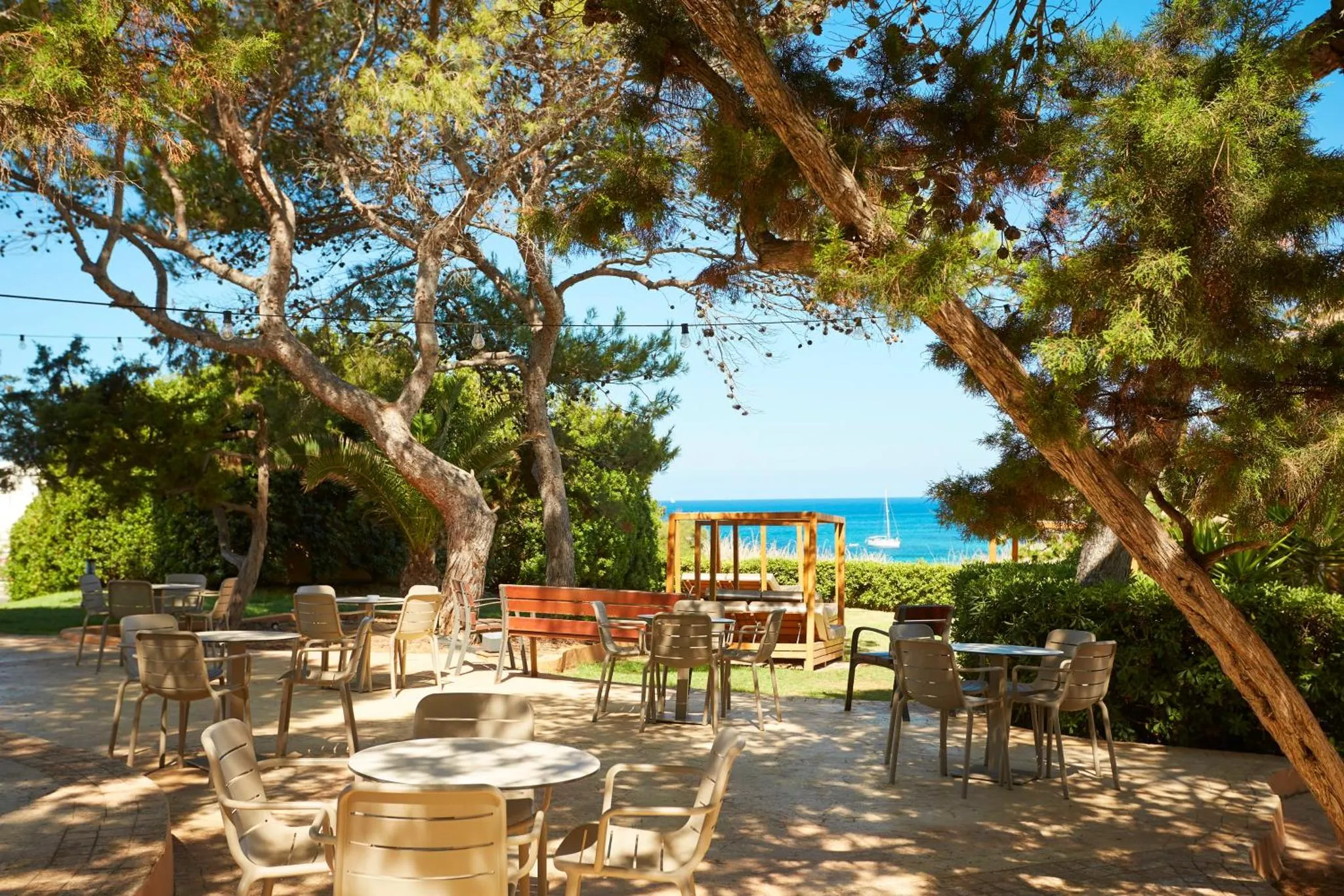 Terrasse ombragée avec tables et chaises donnant sur la mer.