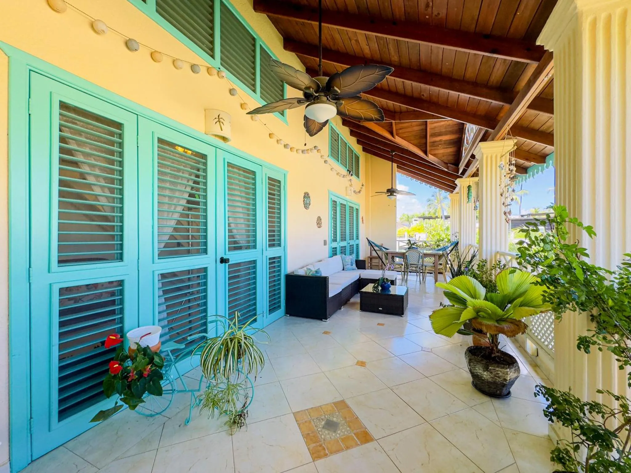 Terrasse ombragée avec mobilier de jardin et plantes tropicales.