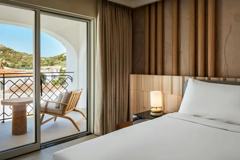 Une chambre lumineuse s'ouvre sur un balcon avec vue sur la végétation.