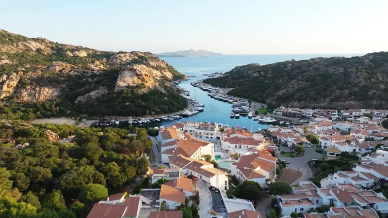 Vue aérienne d'une marina bordée de bâtiments blancs et de collines verdoyantes.