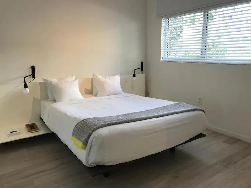 Une chambre lumineuse avec un grand lit recouvert d'une courtepointe grise.