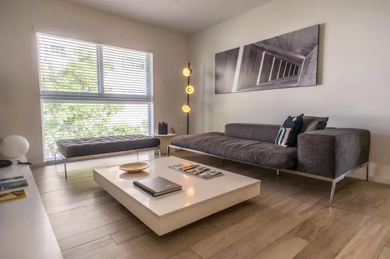 Un salon moderne avec canapé gris, table basse blanche et grande fenêtre.