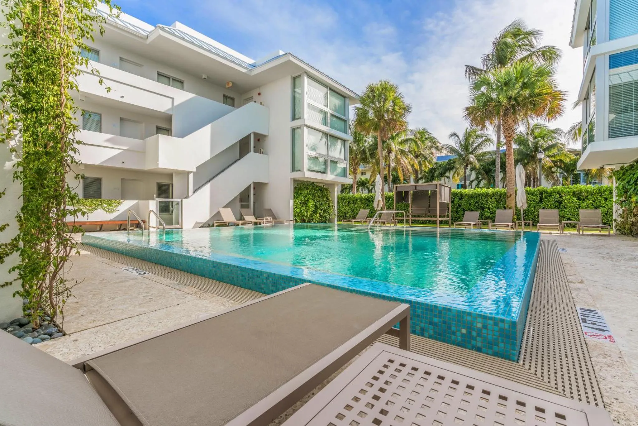Une piscine rectangulaire bordée de transats et de végétation tropicale.