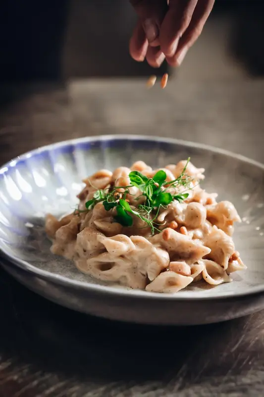 Une assiette de pâtes crémeuses est garnie de quelques herbes et de noix.
