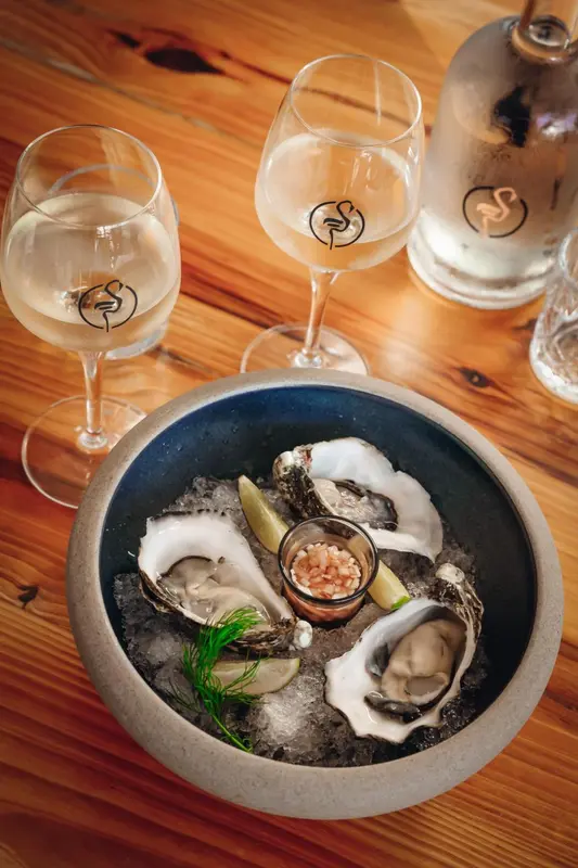 Une assiette d'huîtres fraîches est présentée sur une table en bois, entourée de verres à vin.