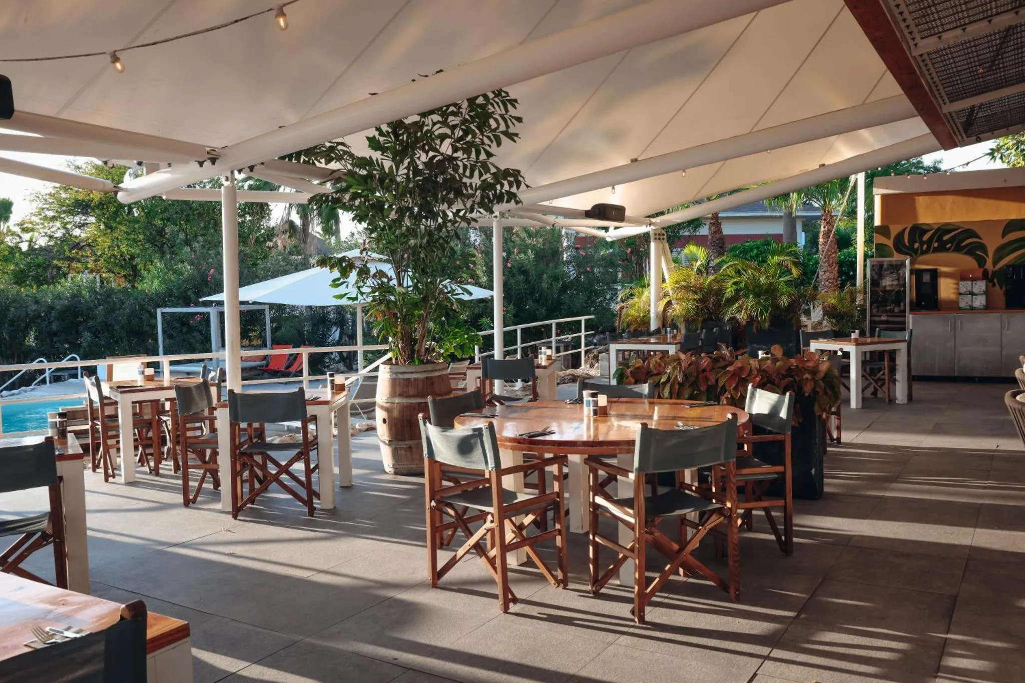Terrasse ombragée avec tables et chaises en bois près d'une piscine.