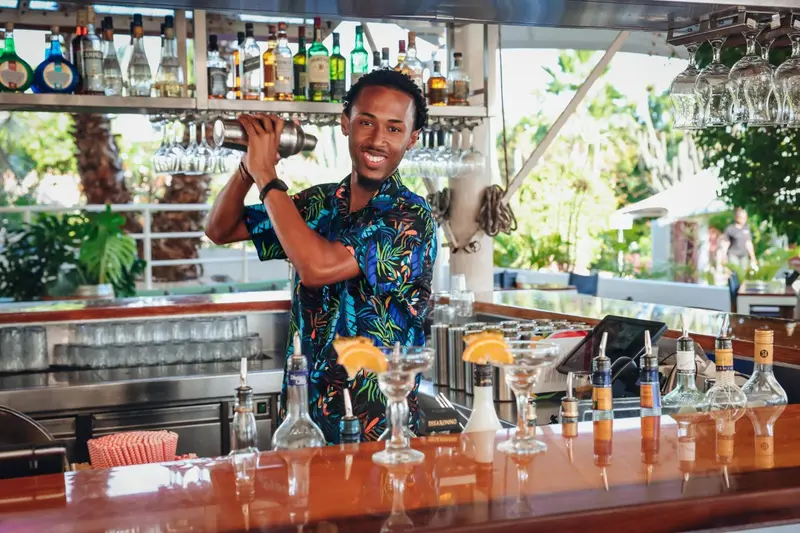 Un barman prépare un cocktail derrière un comptoir bien garni.