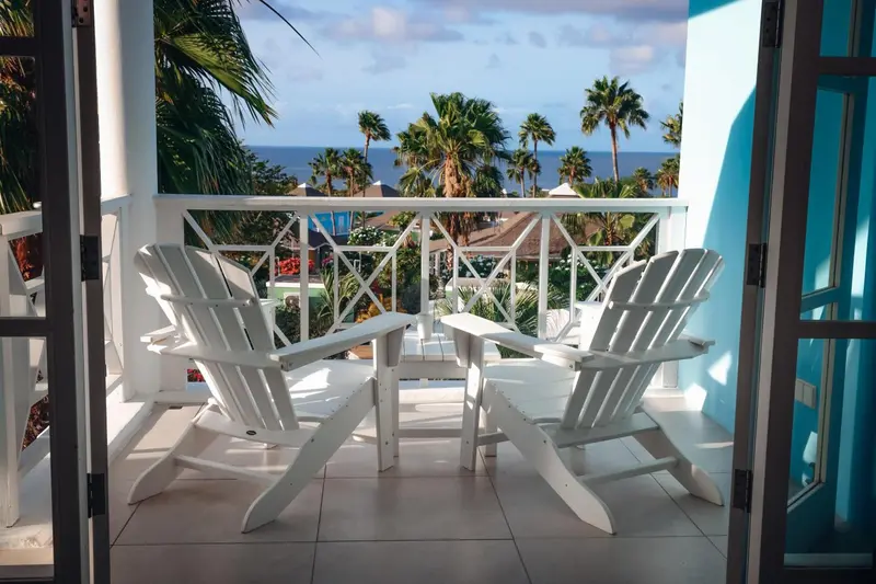 Deux fauteuils blancs sur une terrasse ensoleillée avec vue sur la mer et la végétation.