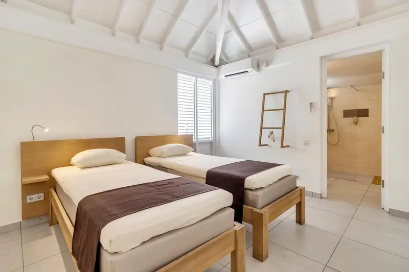 Une chambre lumineuse avec deux lits simples et une salle de bain attenante.
