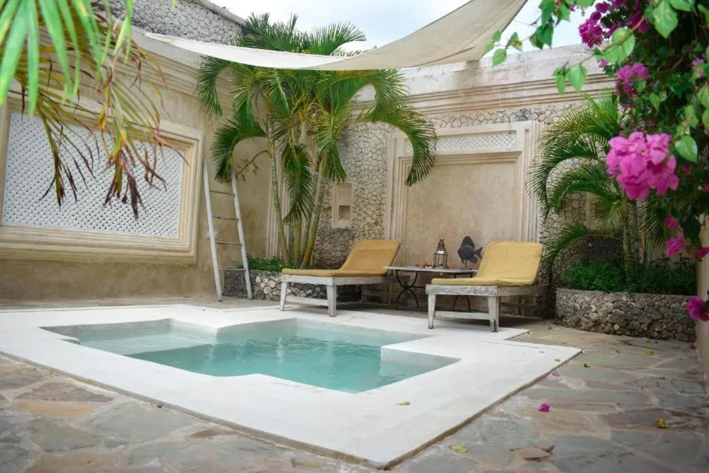 Petite piscine et chaises longues dans une cour ombragée par des plantes.