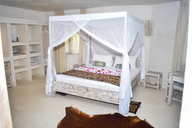 Une chambre lumineuse avec un lit à baldaquin décoré de moustiquaire et de pétales de fleurs.