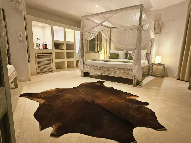 Une chambre lumineuse avec un grand lit à baldaquin et une peau de vache au sol.