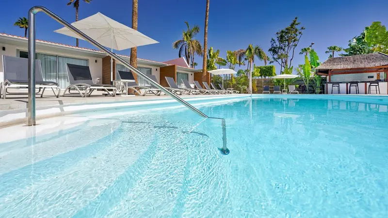 Transats alignés au bord d'une piscine turquoise sous un ciel bleu.