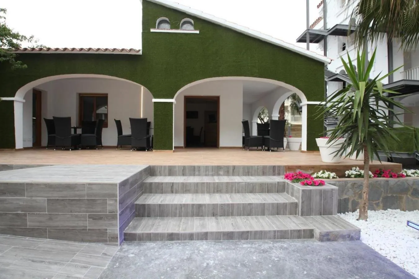 Terrasse ombragée avec mobilier de jardin devant un bâtiment.