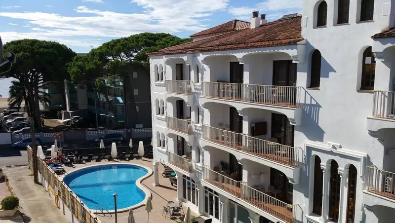 Bâtiment blanc à plusieurs étages avec des balcons et une piscine en contrebas.