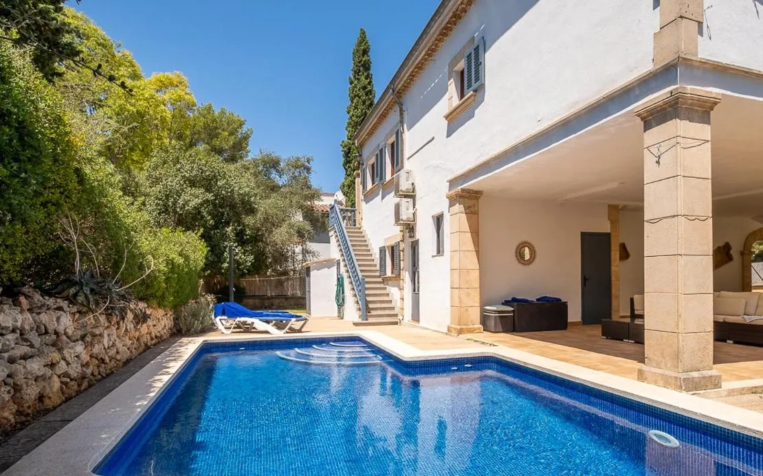 Une piscine rectangulaire est bordée d'une terrasse avec des transats et un bâtiment aux colonnes.