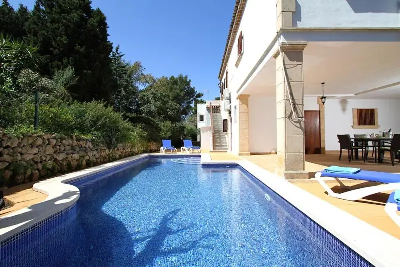 Une piscine rectangulaire avec des chaises longues se trouve devant un bâtiment en pierre.