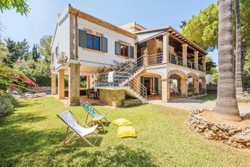 Villa blanche avec terrasse et jardin verdoyant ensoleillé.