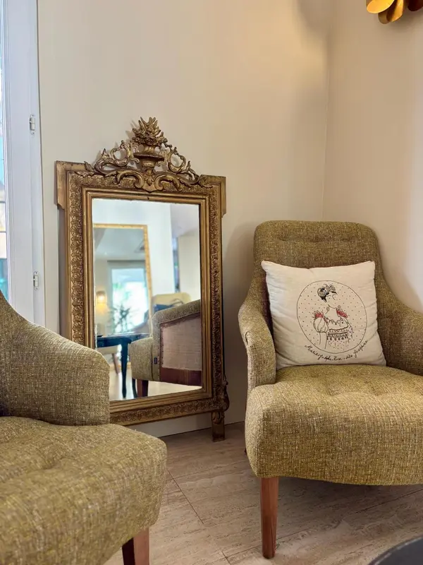 Un fauteuil vert olive se trouve à côté d'un grand miroir doré.