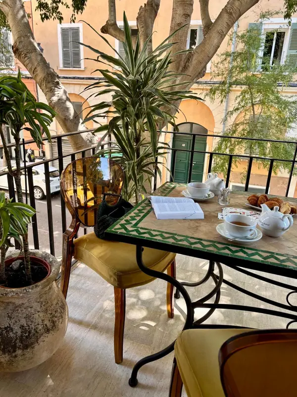 Une table avec une tasse de thé et des pâtisseries sur un balcon ensoleillé.
