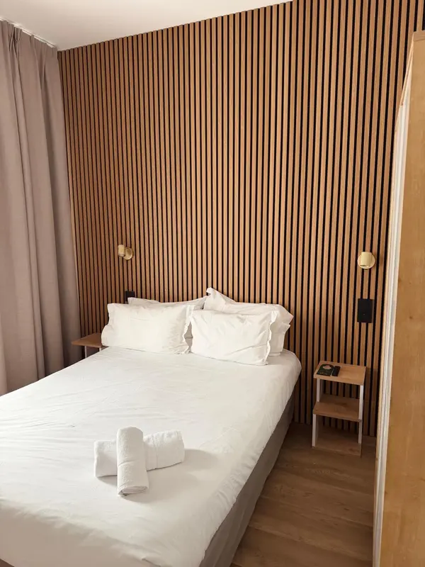 Une chambre lumineuse avec un lit recouvert d'une couette blanche et des tables de chevet en bois.