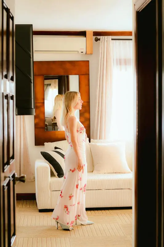 Une femme se tient dans une chambre lumineuse avec un canapé blanc et un grand miroir.