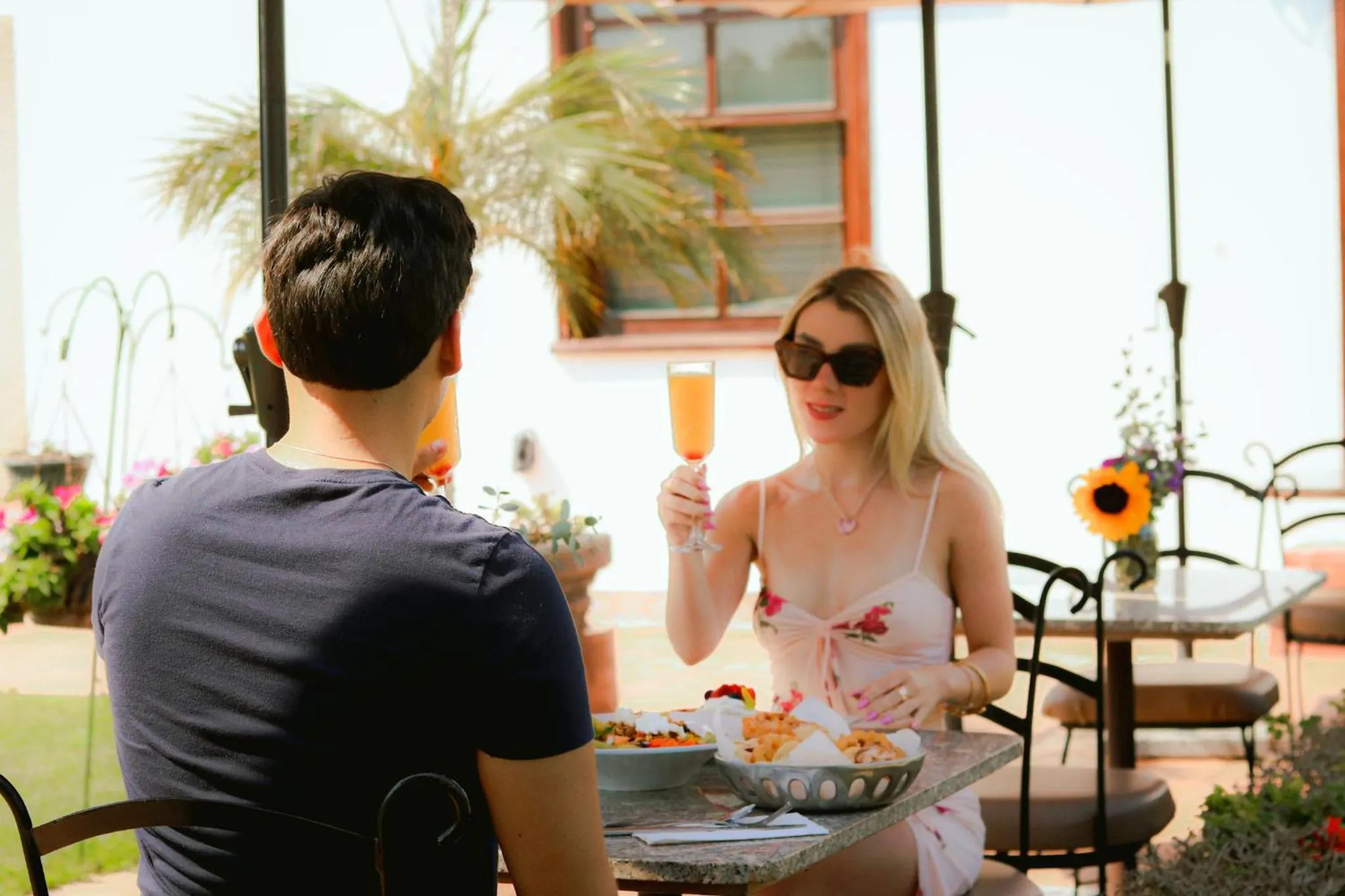 Une femme et un homme sont assis à une table en terrasse et dégustent des boissons et un repas.