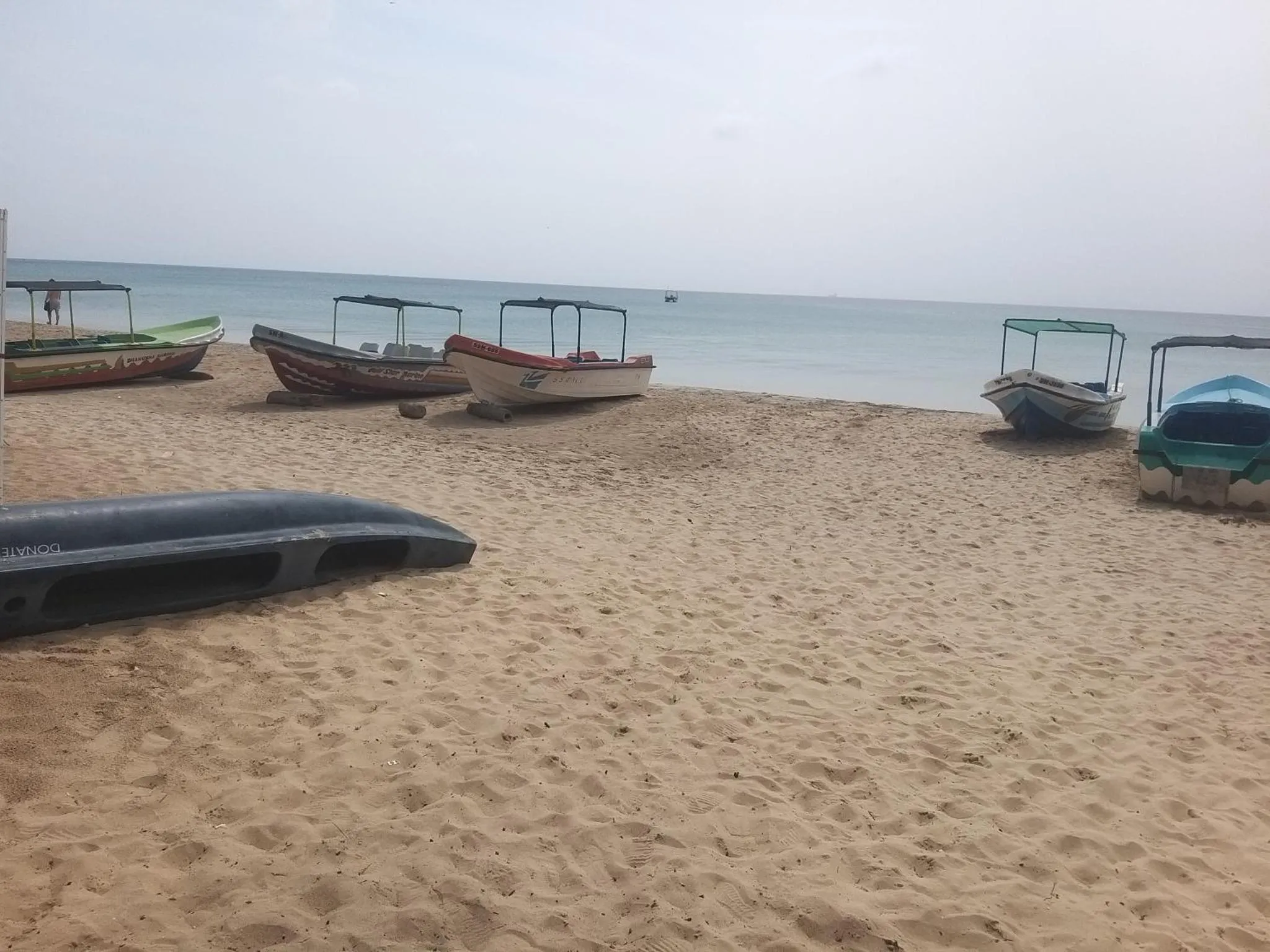 Plusieurs embarcations colorées reposent sur une plage de sable fin face à la mer.