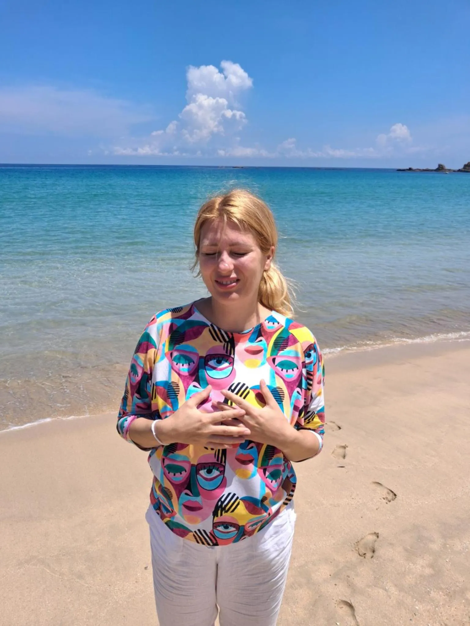 Une femme se tient sur une plage de sable clair, face à la mer.