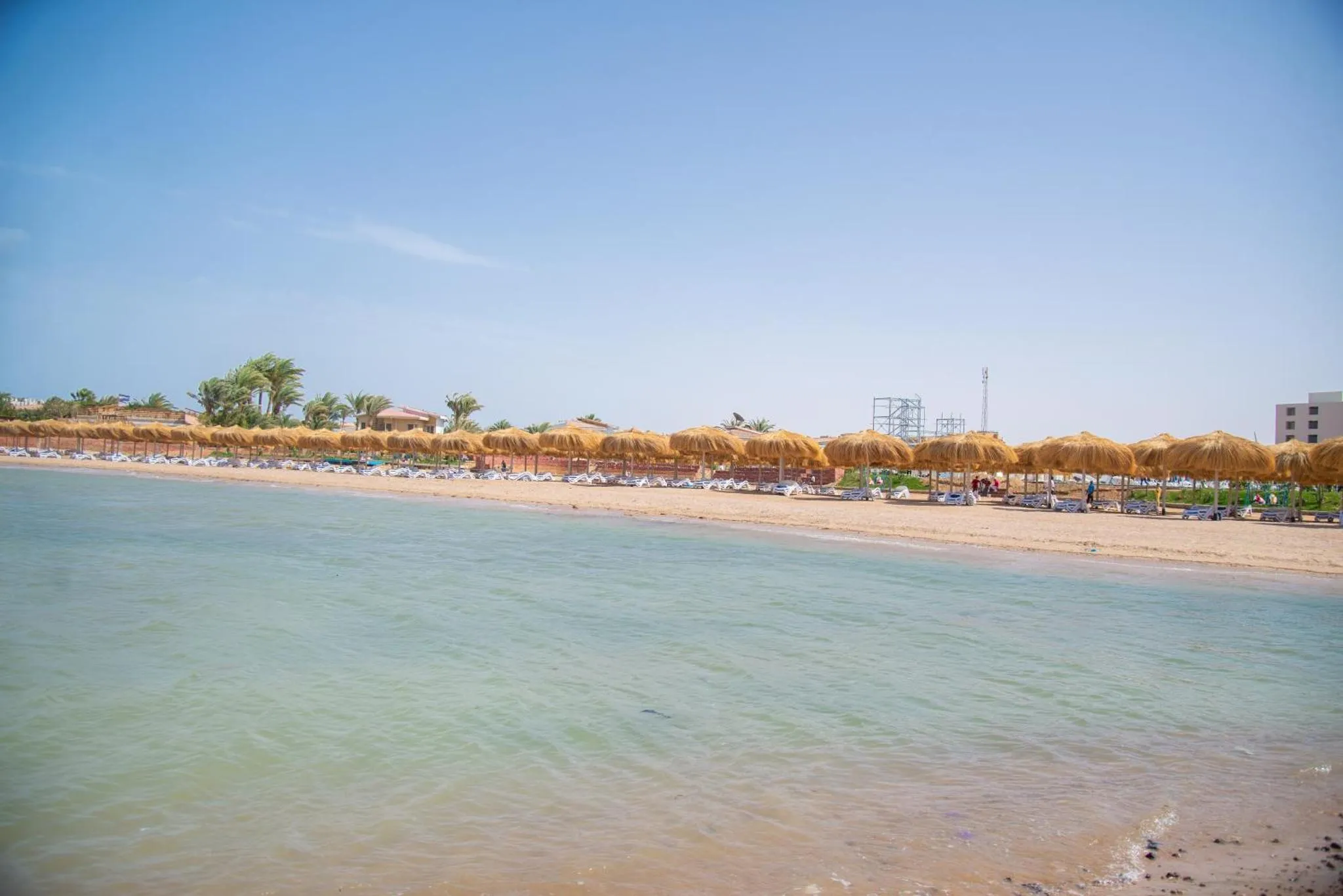 Plage de sable fin avec transats et parasols sous un ciel bleu.